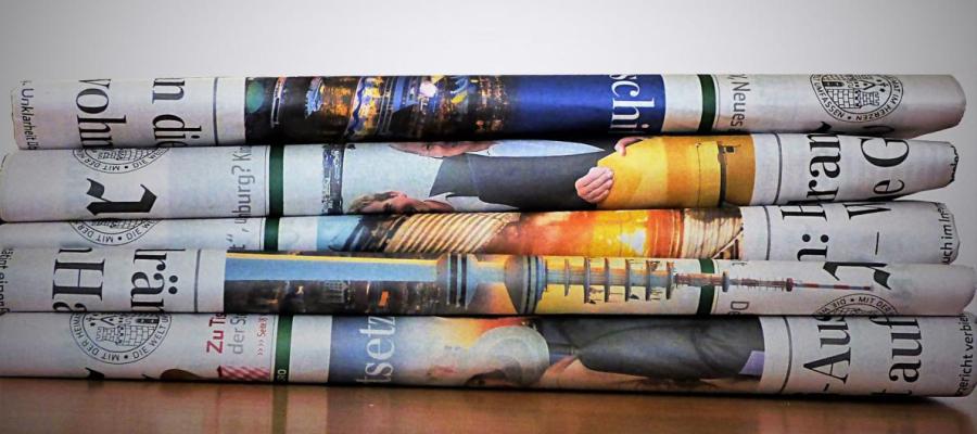 A pile of folded broadsheet newspapers on a desk