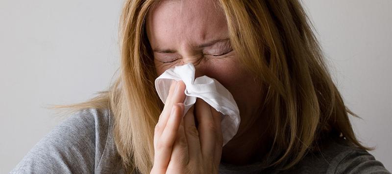 Woman sneezing into a tissue